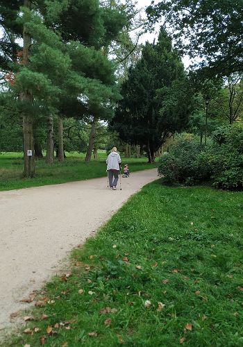 Frau auf Krücken  und Kind auf Laufradim Park unterwegs